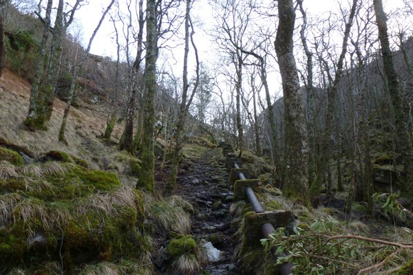 Path by metal pipeline ascending to dammed lochan